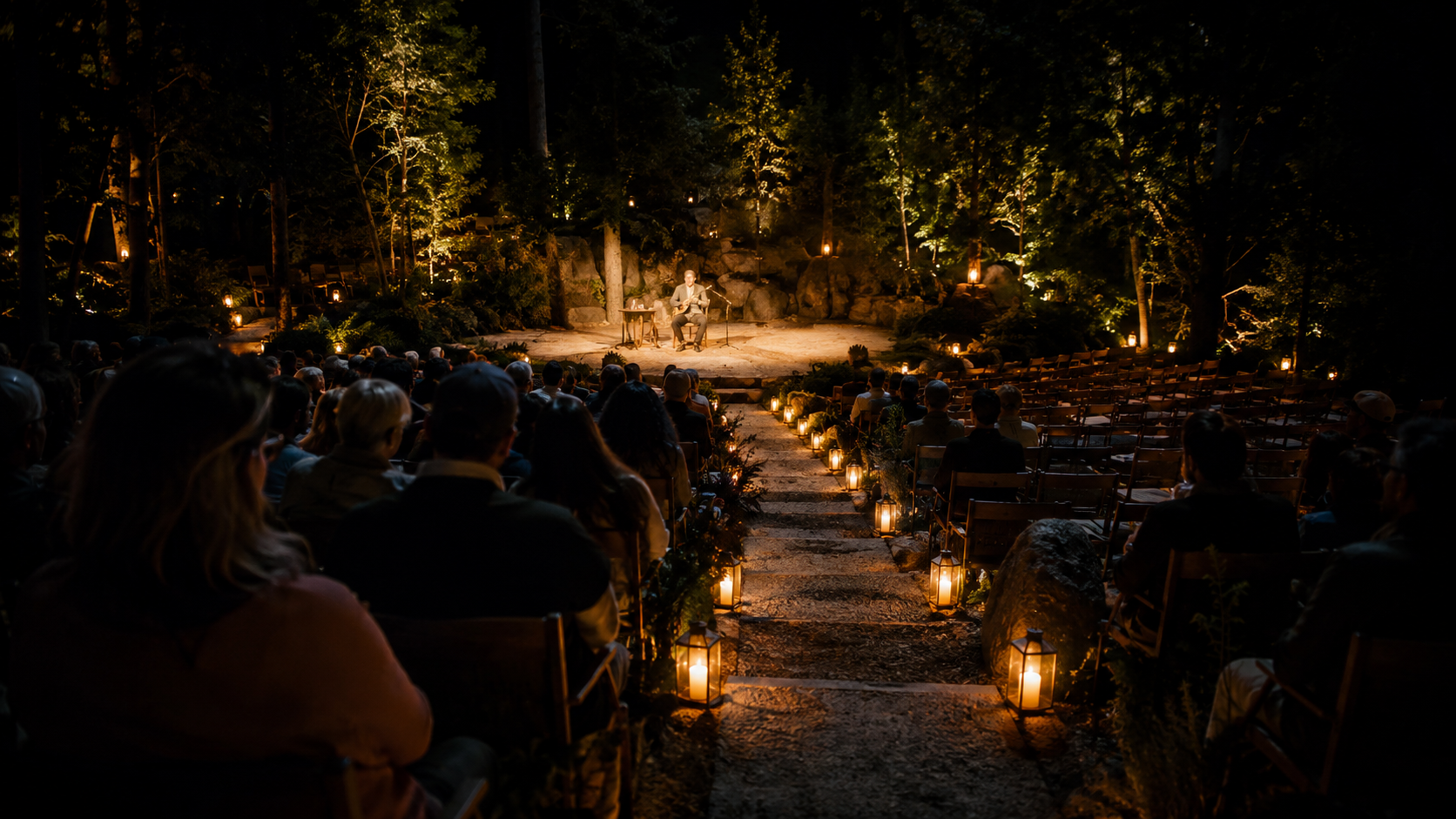 An outdoor audience gathers for a performer on a small stage, with lanterns leading toward the show.